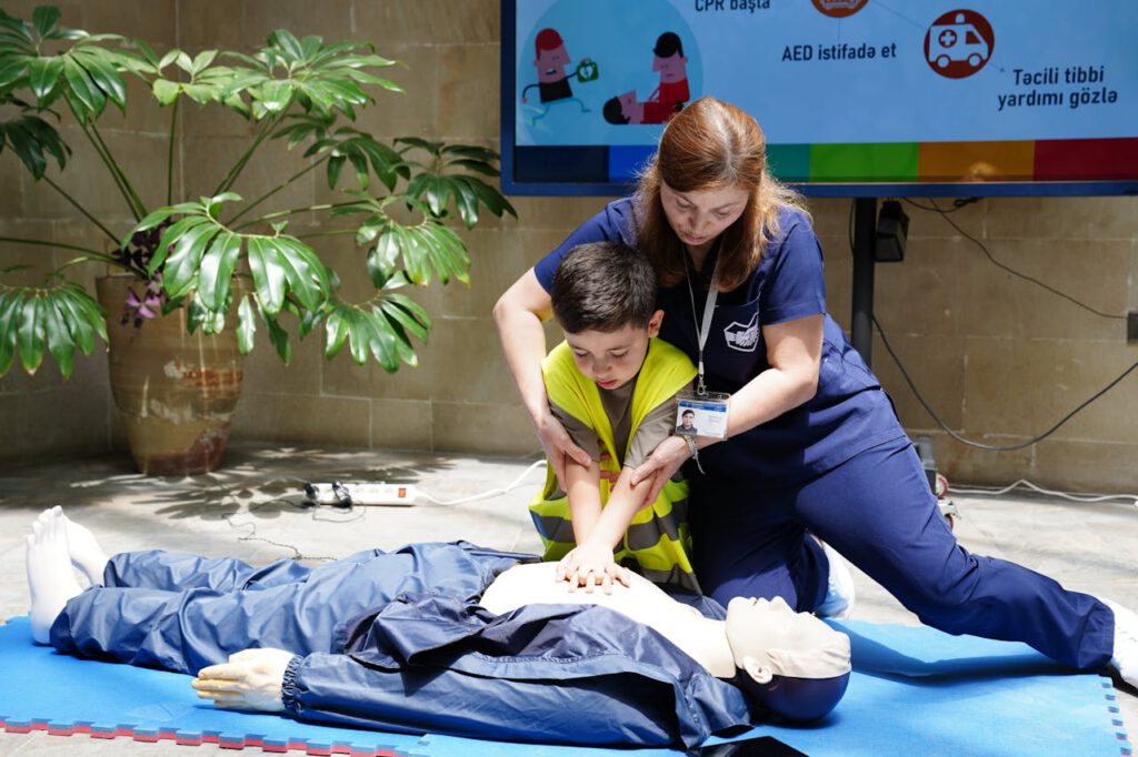 Nurse guides child in CPR training using a dummy indoors.