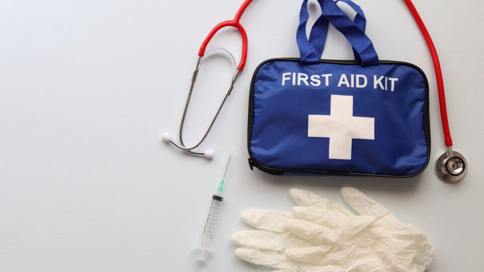 Flat lay of first aid kit, stethoscope, syringe, and gloves on white background.