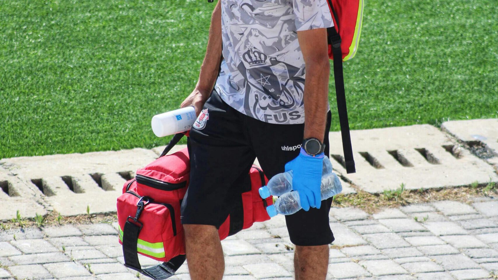 A football medic with emergency gear walking on a sports field, ready for action.